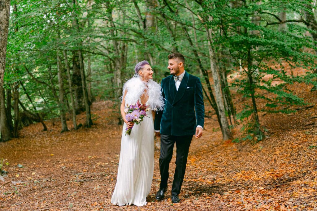 Michele e Martina dopo il loro matrimonio camminano nel bosco. Michele indossa una giacca in velluto verde petrolio di Scabal, simbolo di eleganza e raffinatezza, perfettamente in armonia con l’atmosfera naturale.