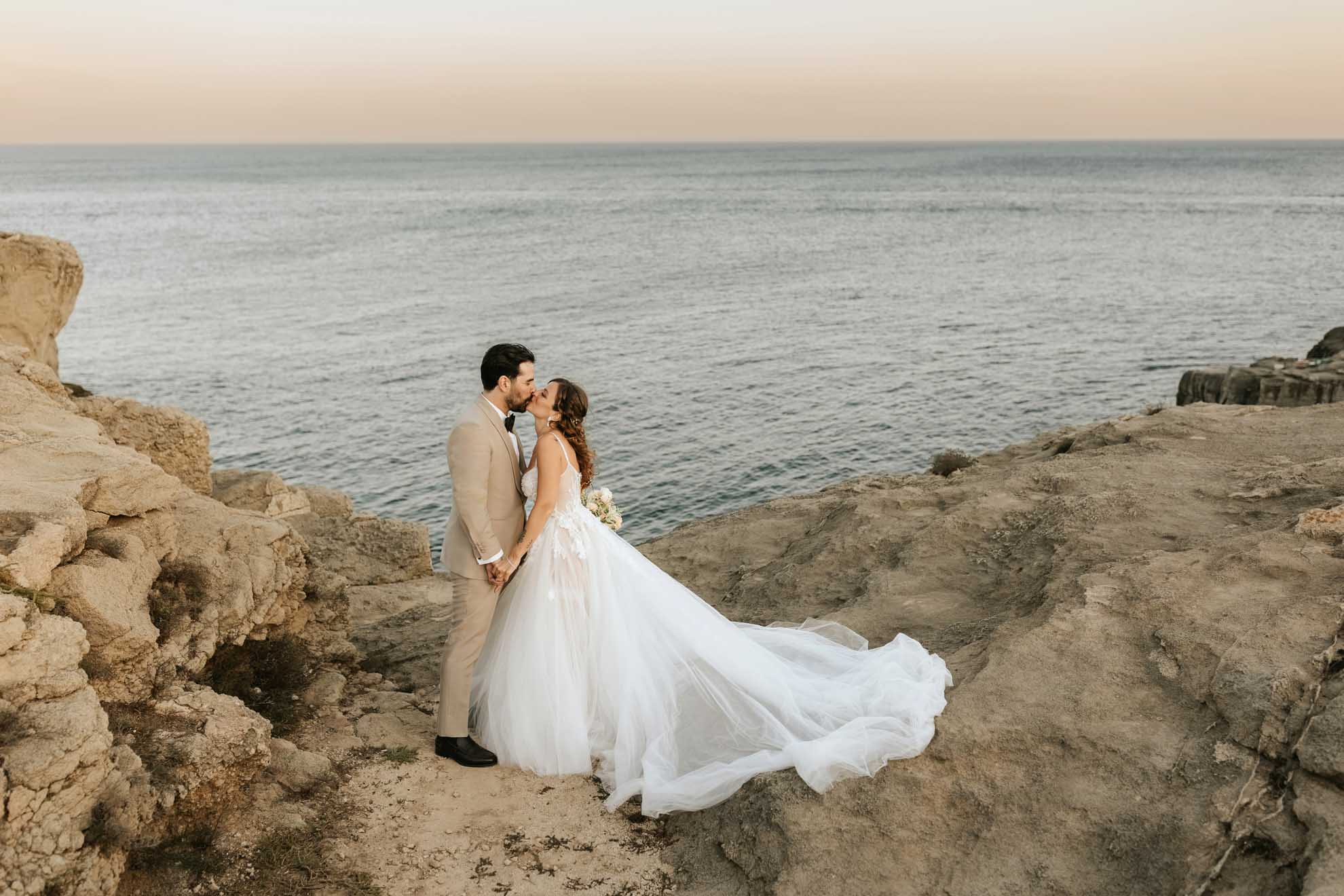 Simone, nel suo abito sabbia sartoriale, e Chiara si baciano di fronte al mare, simbolo del loro amore senza confini.