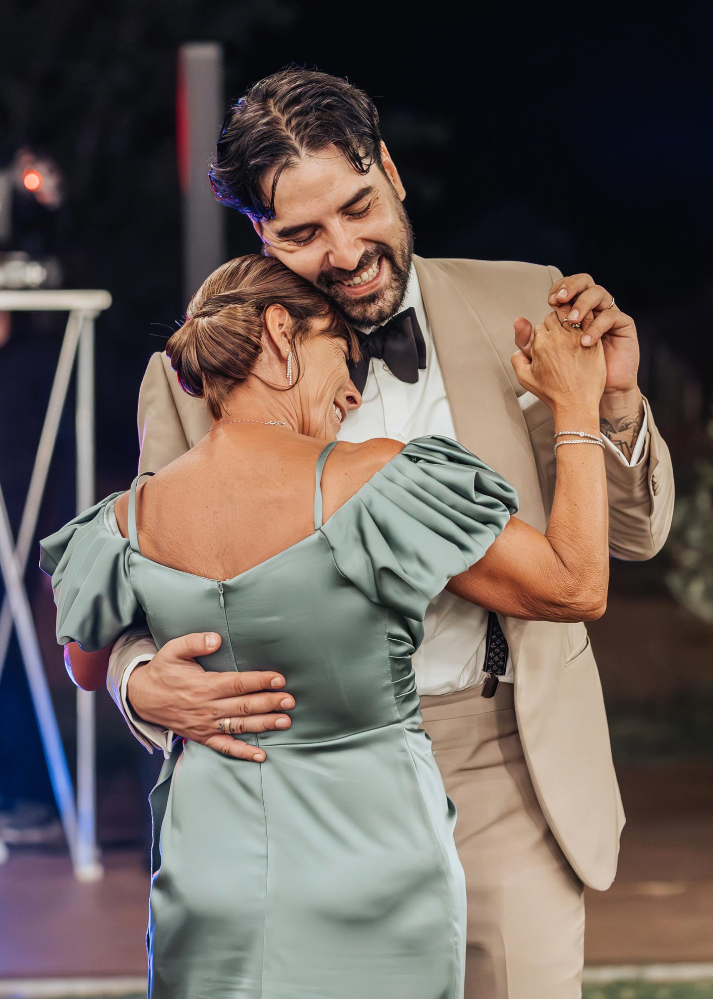 Simone balla con sua madre durante il ricevimento, indossando un elegante abito su misura color sabbia, simbolo di raffinatezza e cura sartoriale.